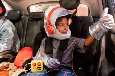 Un enfant écoute son Yoto Mini avec un casque sur la banquette arrière d'une voiture