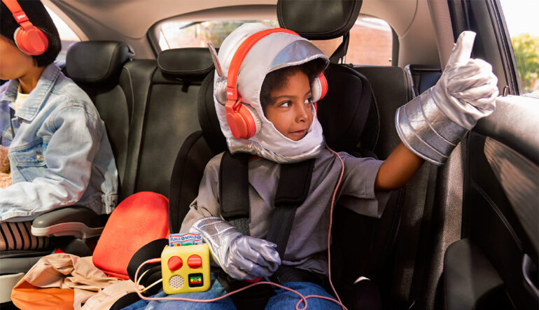 Un enfant écoute son Yoto Mini avec un casque sur la banquette arrière d'une voiture