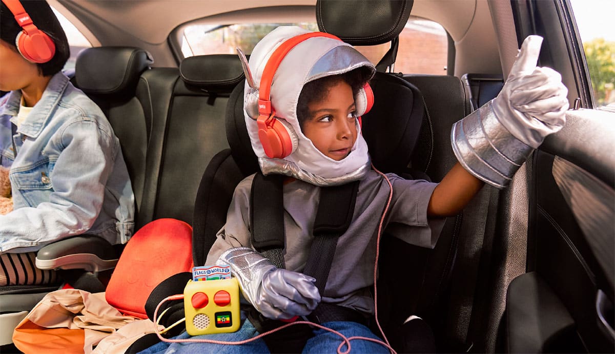 Un enfant écoute son Yoto Mini avec un casque sur la banquette arrière d'une voiture