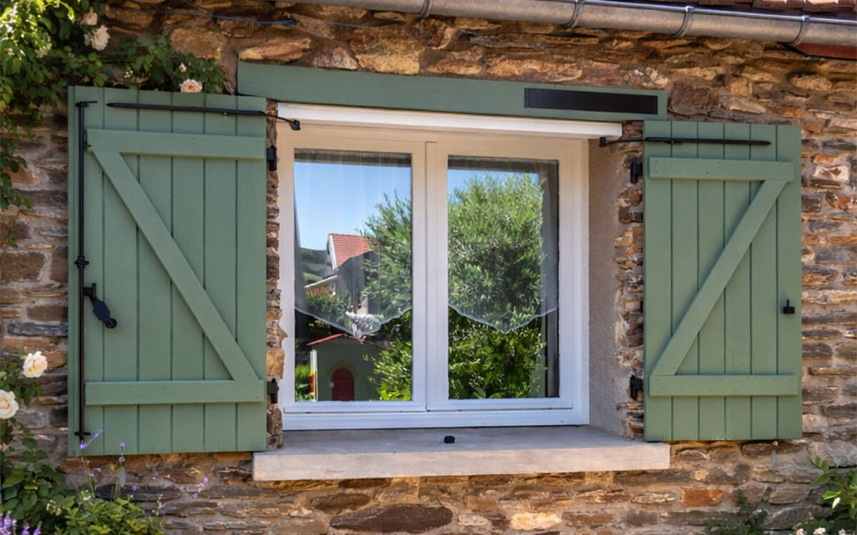 Motorisation solaire SLID'UP WINEO installée sur des volets battants verts d'une maison de campagne